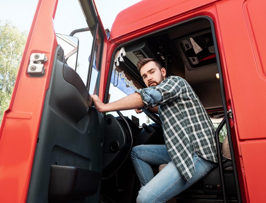 Handsome bearded truck driver inside his red cargo truck Handsome bearded truck driver sitting inside his red cargo truck